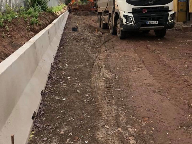 Jersey barriers lining both sides of a muddy haul road with a tipper lorry
