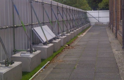 Site hoarding braced onto kentledge blocks along a paved walkway