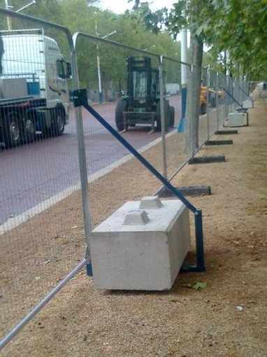 Temporary mesh fencing braced by concrete ballast blocks along a paved route