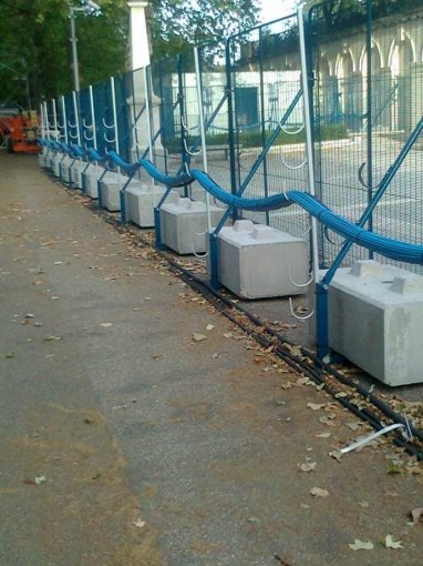 Mesh fence panels each footed on a concrete ballast block outside a historic building