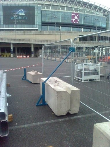 Temporary fence panels braced with concrete kentledge blocks outside a stadium