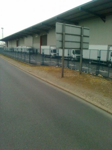 Mesh fencing weighted with concrete ballast blocks beside a distribution warehouse