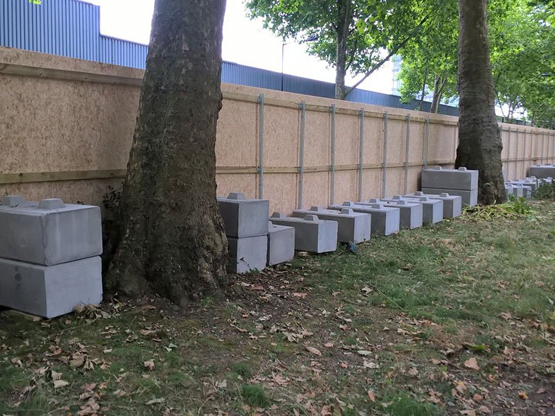 Row of kentledge blocks set along the base of a site hoarding