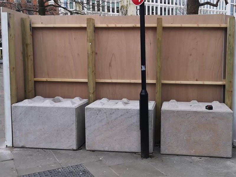 Three kentledge blocks ballasting a timber site hoarding on a pavement