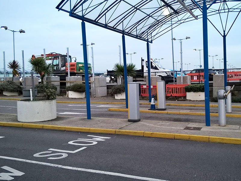 Precast bollards and planters lining a canopied access road marked slow