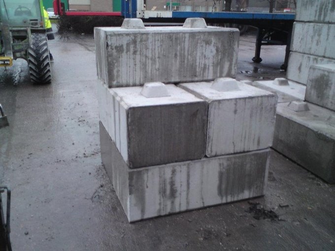 Kentledge ballast blocks stacked on a wet quayside beside a tractor