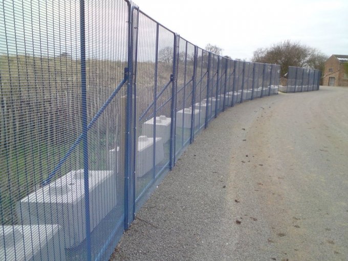 Blue mesh security fencing anchored by concrete ballast blocks along a track