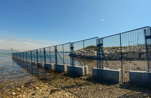 Kentledge ballast blocks anchoring temporary security fencing along a shoreline