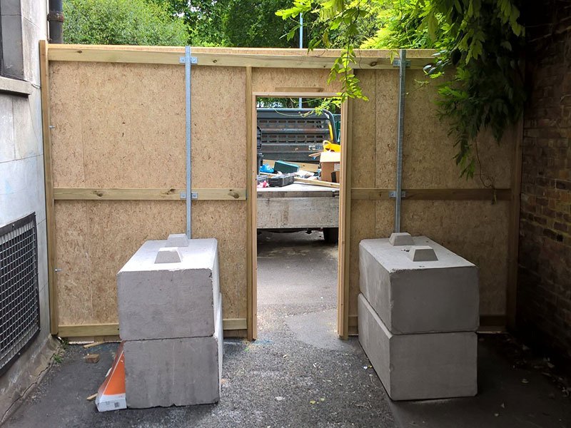 Kentledge blocks anchoring timber hoarding panels either side of a site opening