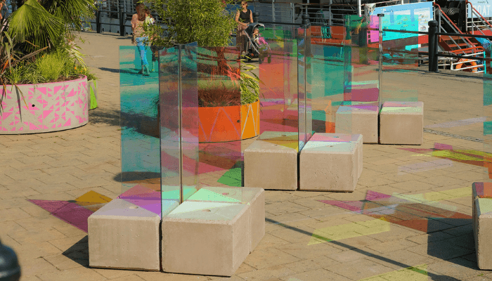 Concrete block seating among coloured glass panels on a paved quayside