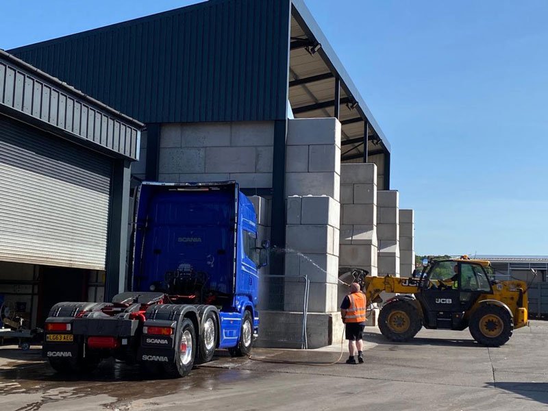 Articulated lorry and telehandler beside interlocking block material bays at an industrial unit