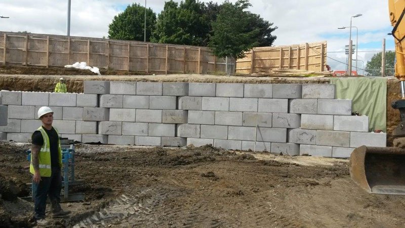 Worker beside a long Legato block wall under construction on site