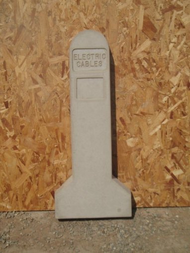 Indicator post cast with Electric Cables lettering propped against a plywood board