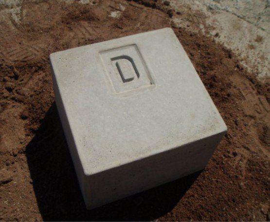 Concrete marker block stamped with a letter D resting on bare soil