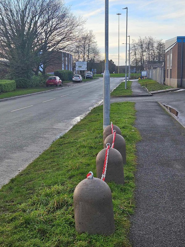 Line of chained concrete bollards guarding a grass verge beside a road