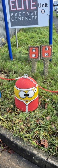 Concrete bollard painted as a festive character on a verge beside a site sign