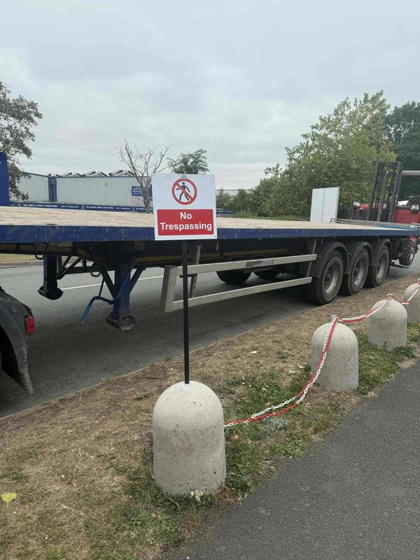 Chained concrete bollards with a no trespassing sign beside a parked trailer