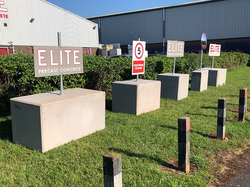 Concrete signage ballast blocks holding freestanding sign posts on grass