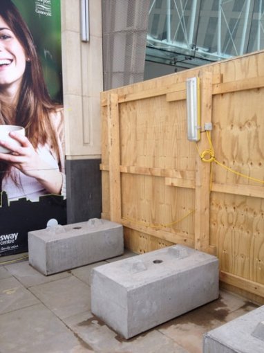 Precast hoarding blocks weighting a timber hoarding panel outside a shopfront