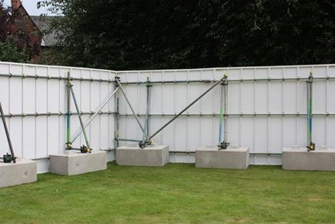 Kentledge blocks weighting a braced hoarding run across a grassed area
