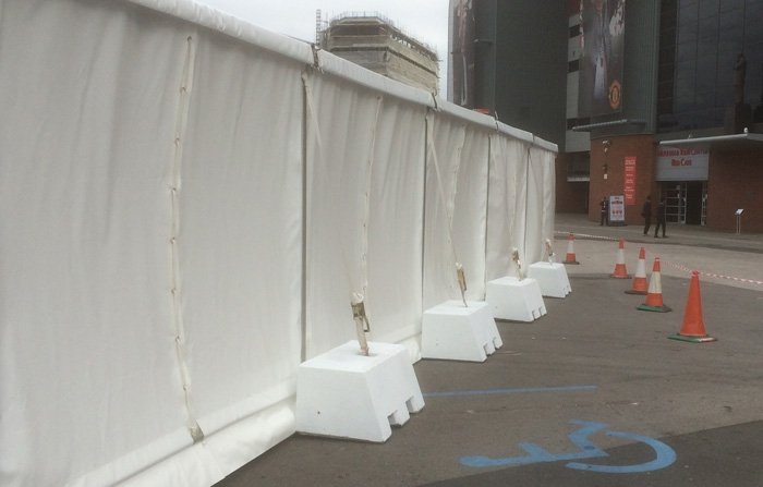 Ballast blocks weighting a white sheeted temporary fence across a paved area