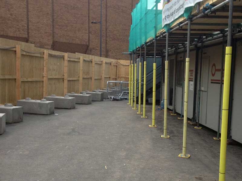 Concrete ballast blocks anchoring a timber hoarding run around a building site