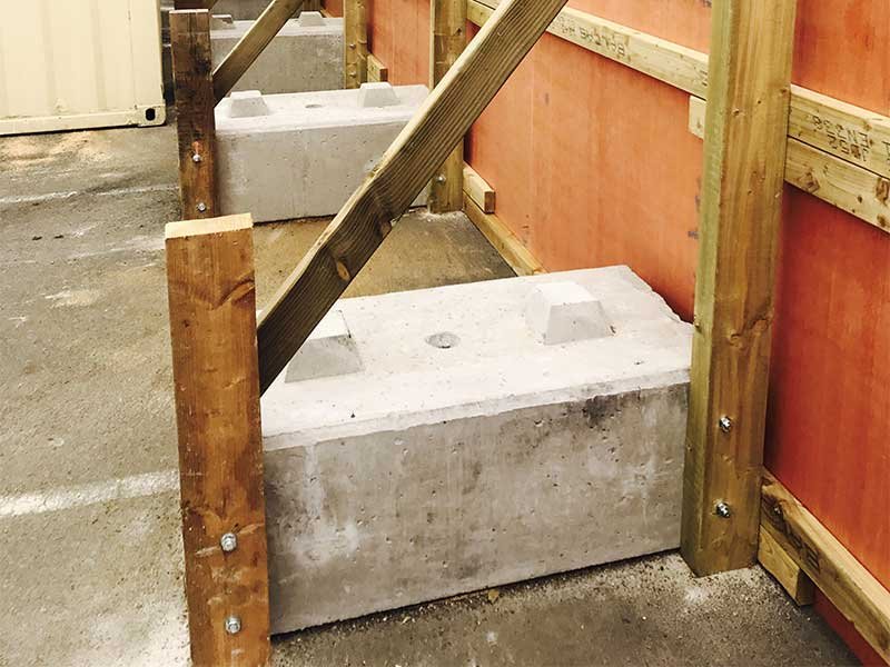 Concrete blocks anchoring the timber bracing behind a site hoarding panel