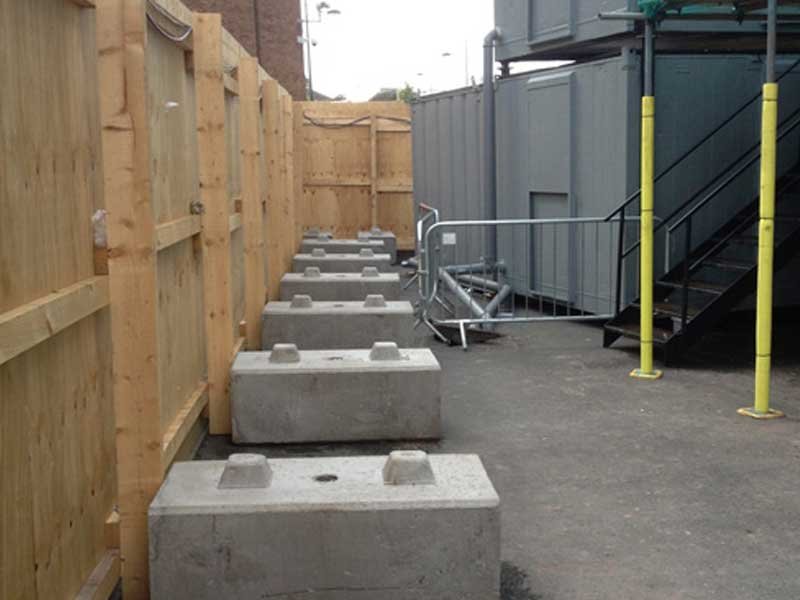 Row of concrete base blocks supporting no-dig timber hoarding panels
