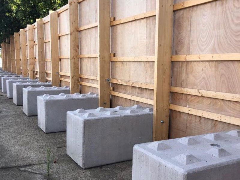 Line of concrete ballast blocks supporting tall plywood hoarding panels
