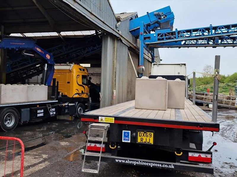 Lorry-mounted crane offloading precast blocks from a flatbed trailer at a plant