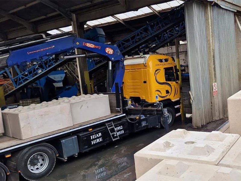 Lorry-mounted crane offloading Legato blocks from a flatbed under a factory canopy