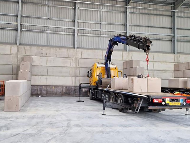 Lorry-mounted crane offloading interlocking blocks inside a warehouse bay