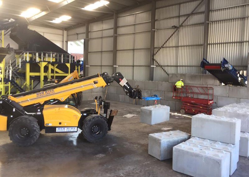 Telehandler placing interlocking blocks for waste bays inside a processing shed