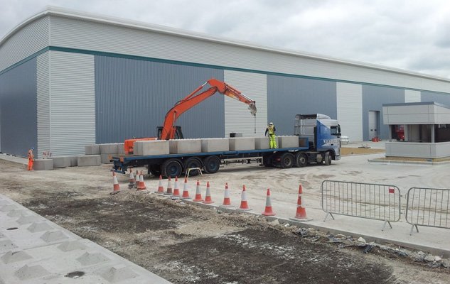 Lorry-mounted grab unloading interlocking blocks outside a new industrial unit