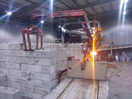Lorry-mounted crane lifting a block onto a storage bay wall inside a shed
