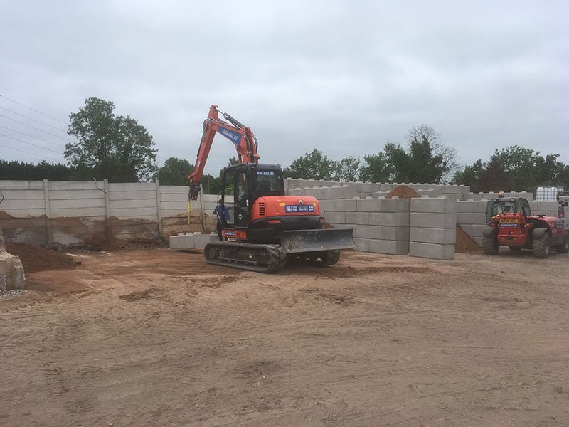Tracked excavator working beside a long interlocking block storage bay wall on a sandy site