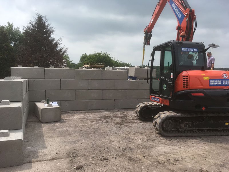Excavator placing Duo blocks to form a storage bay wall in a yard
