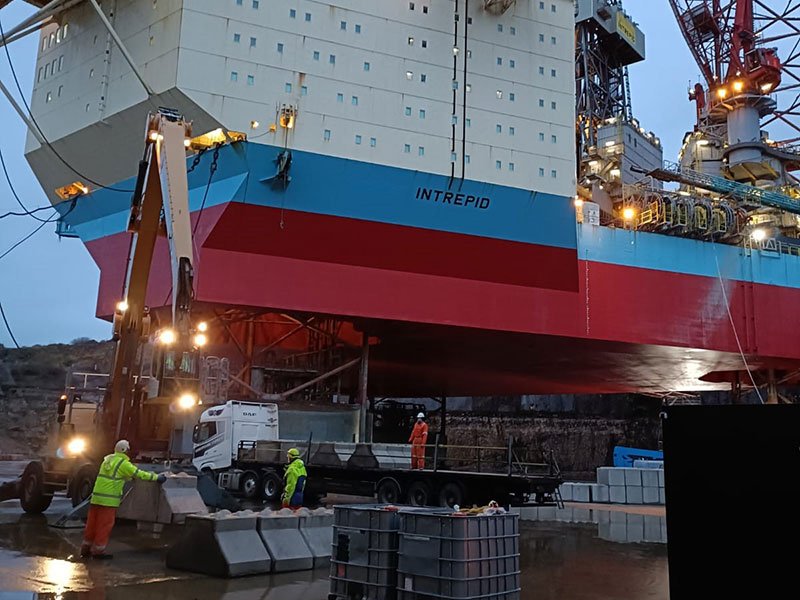 Workers positioning concrete blocks beneath a rig hull at night