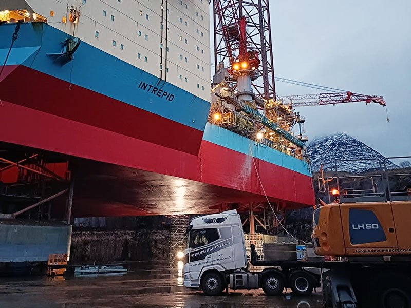 Lorry and crane working beneath a rig hull at a decommissioning yard
