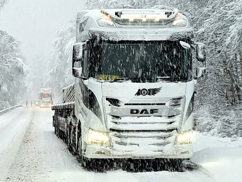 Loaded delivery lorry driving through heavy snow on a tree-lined road