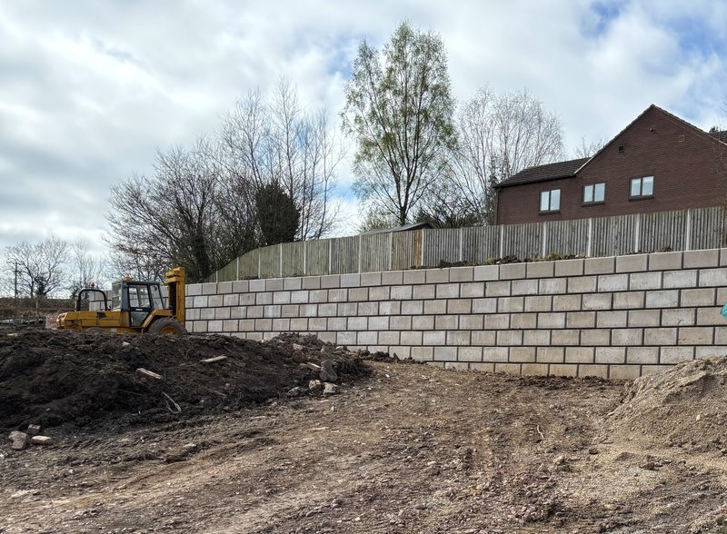 Smooth-faced Retainer-Rock wall behind housing with a digger on cleared ground