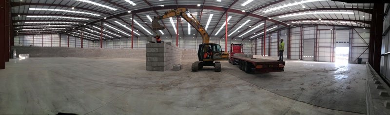 Excavator placing interlocking blocks inside a large empty warehouse