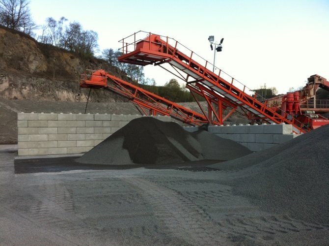 Interlocking block bay walls containing an aggregate stockpile beneath a quarry conveyor