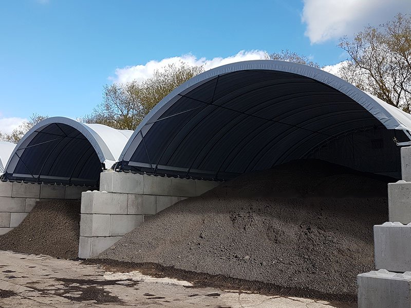Interlocking block walls supporting two fabric-roofed canopies over aggregate stockpiles