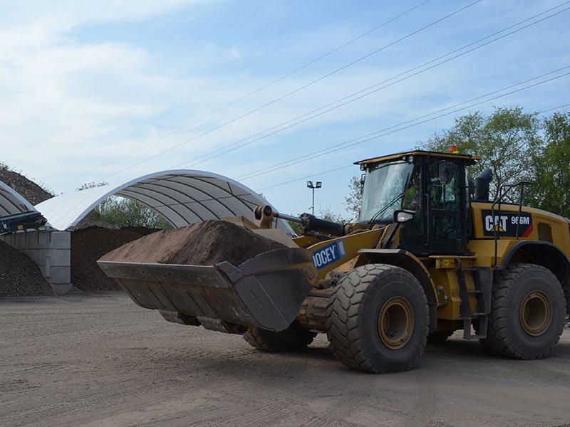 Wheel loader carrying aggregate past a block-walled canopy storage bay