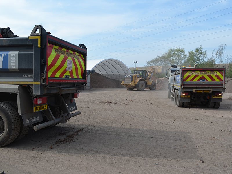 Tipper lorries on a quarry haul road beside block-walled aggregate stores