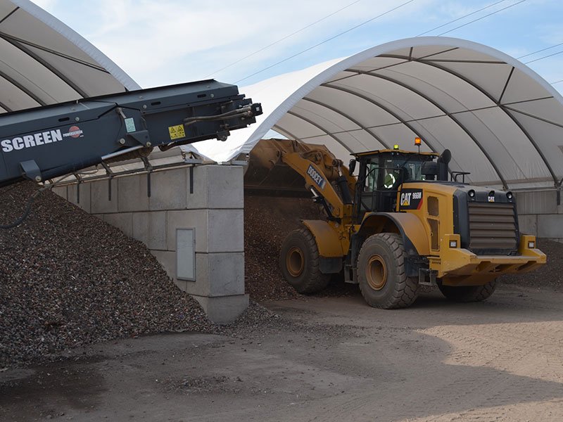 Wheel loader working an aggregate stockpile inside a block-walled canopy store