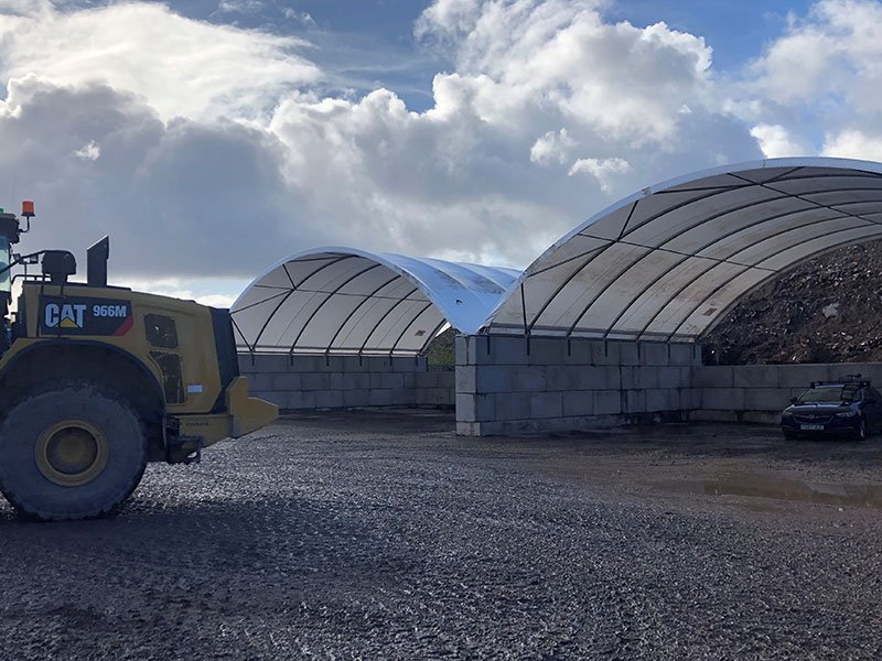 Wheel loader passing two canopy structures built on interlocking block walls