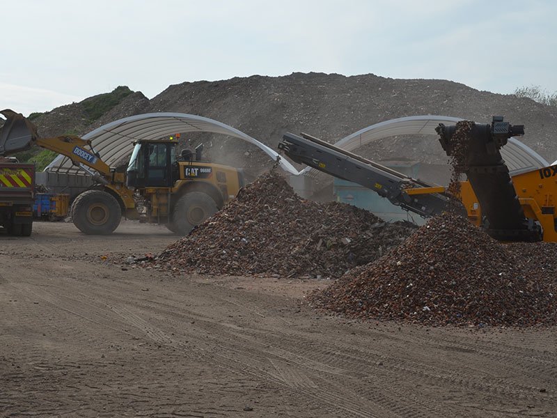 Loaders feeding a screener beside canopy-covered storage bays at a quarry