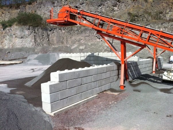 Conveyor stacker discharging aggregate beside an interlocking block bay wall